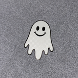 A small embroidered ghost patch with a smiling face, outlined in black, placed on a textured gray fabric background.