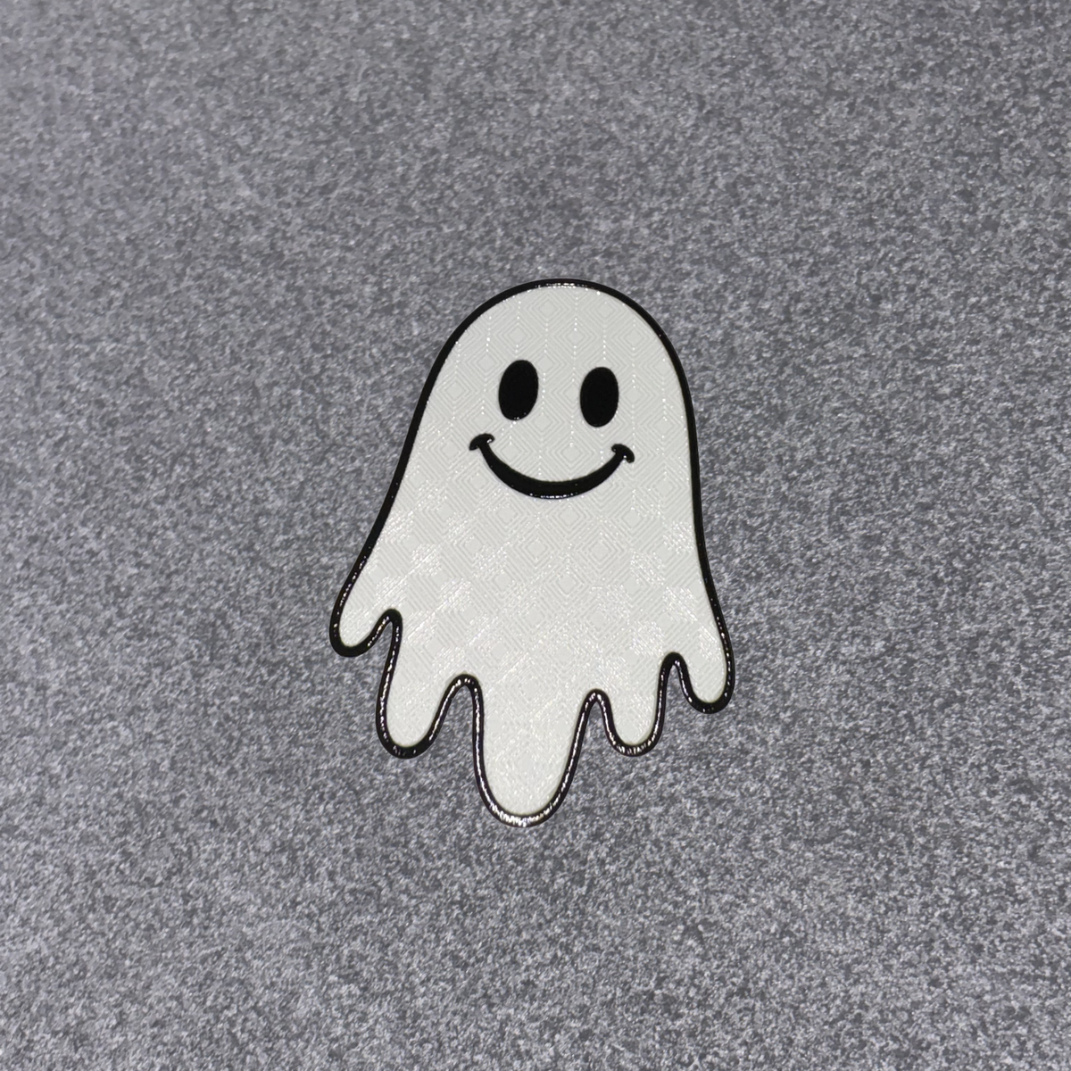 A small embroidered ghost patch with a smiling face, outlined in black, placed on a textured gray fabric background.