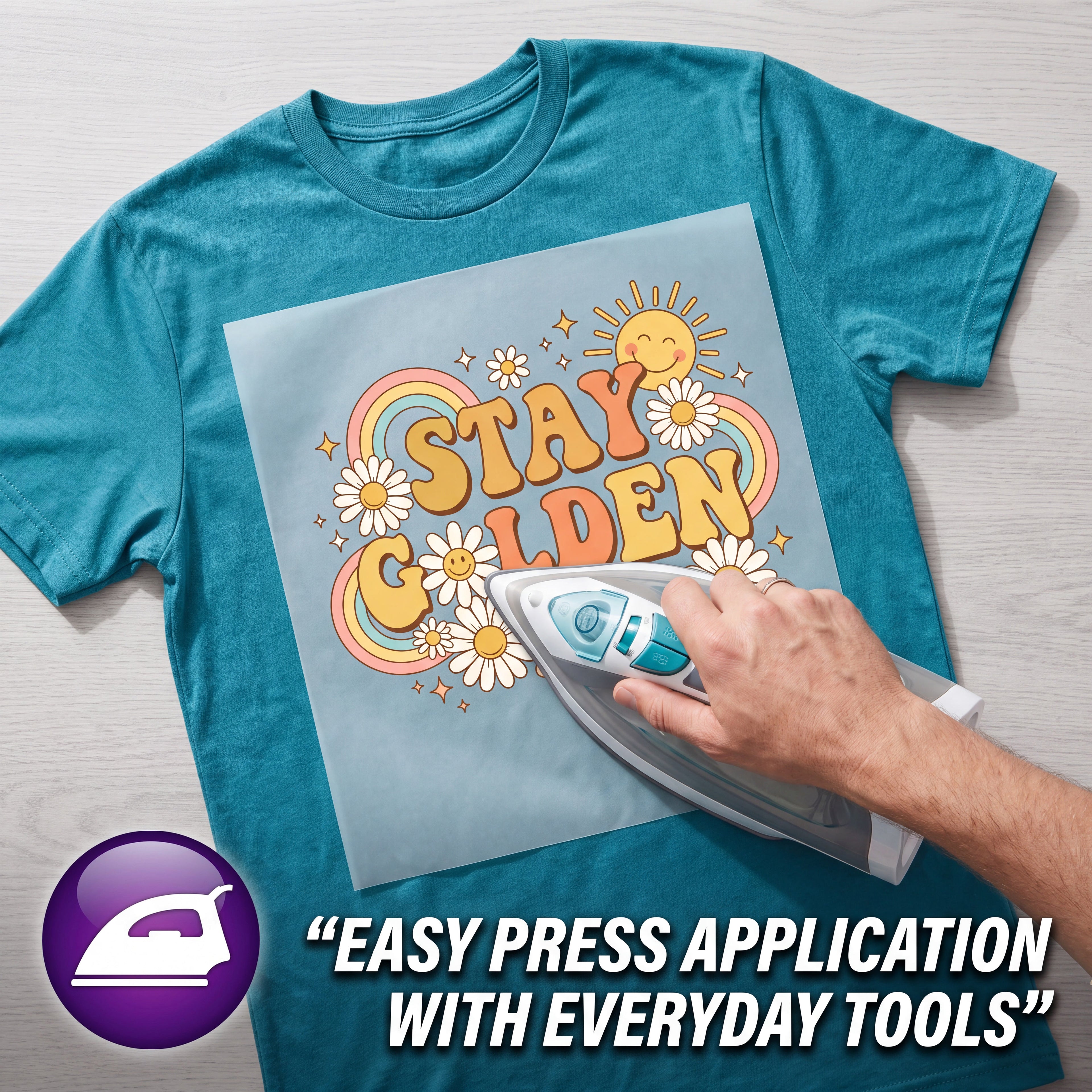 A teal graphic T-shirt laid flat on a light wood surface, with a hand using an iron to apply a light blue heat-press design that reads “Stay Golden” with flowers and a rainbow. A purple icon and the text “EASY PRESS APPLICATION WITH EVERYDAY TOOLS” appear in the lower left and lower right.