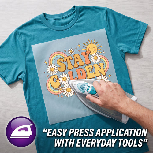 A teal graphic T-shirt laid flat on a light wood surface, with a hand using an iron to apply a light blue heat-press design that reads “Stay Golden” with flowers and a rainbow. A purple icon and the text “EASY PRESS APPLICATION WITH EVERYDAY TOOLS” appear in the lower left and lower right.