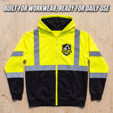 A high-visibility workwear zip-up hoodie laid flat on a light wood background, with reflective yellow panels, gray reflective stripes on the shoulders and sleeves, a black lower body, and a black hood lining. A black and gold IronClad CKEB logo is printed on the left chest.