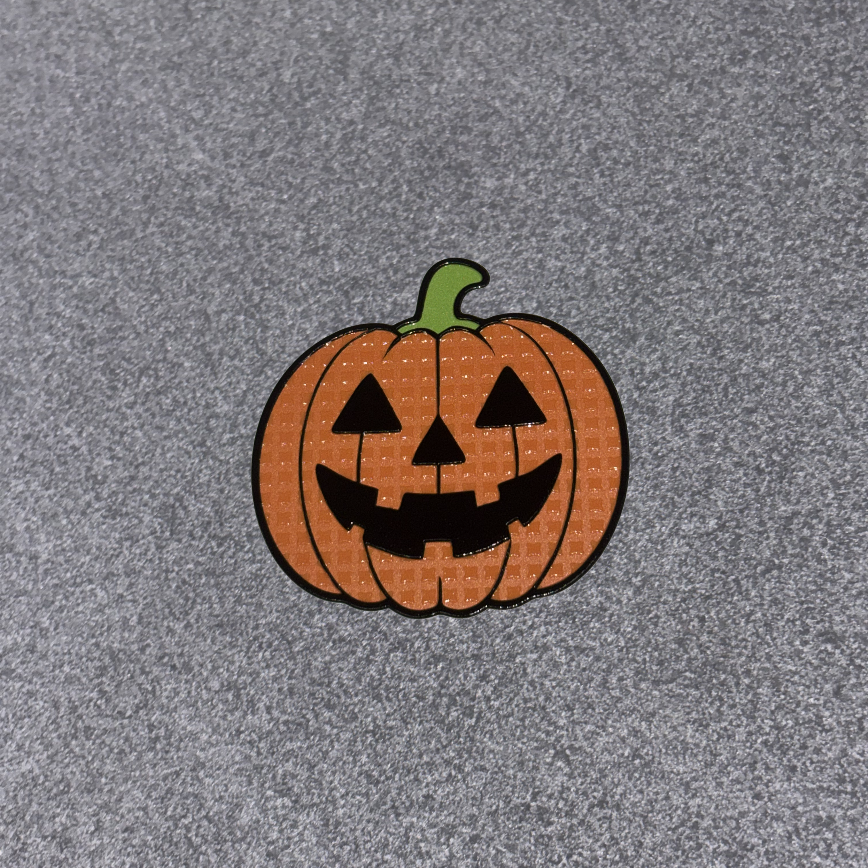 A small embroidered pumpkin patch with a carved jack-o'-lantern face on a textured gray background.