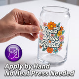 A clear glass can-shaped tumbler with a colorful floral design and the phrase 'Good Days Ahead' in white script, shown on a white surface. A hand is touching the tumbler, and a purple icon plus text at the bottom read 'Apply by Hand' and 'No Heat Press Needed'.