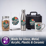 A promotional product display showing a branded 'Palm City Social' logo on multiple items: a glass jar filled with granola, a clear acrylic sign, a stainless steel water bottle, a black hard case, and a white ceramic mug. Text at the bottom reads 'Made for Glass, Metal, Acrylic, Plastic & Ceramic' with small icons indicating compatible materials.