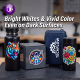 Four insulated containers displayed together on a dark tabletop: a matte black bottle with a colorful tiger graphic, a dark gray box with a circular astronaut graphic, a navy hard case with TECHFLOW branding, and a black canister with a multicolor floral design. Large promotional text at the top reads, 'Bright Whites & Vivid Color Even on Dark Surfaces.